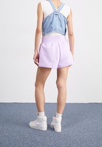Lila bomullsshorts med sidofickor, avslappnad passform, i kombination med en kort denimväst. Vita hög-top sneakers fulländar outfiten.