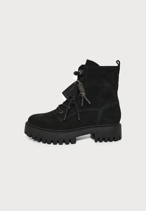 Botte de combat en daim noir à lacets avec semelle épaisse striée et étiquette de marque attachée aux lacets, vue de côté extérieur sur fond uni.