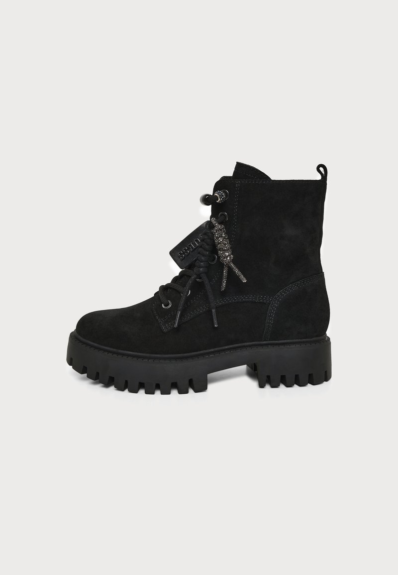 Botte de combat en daim noir à lacets avec semelle épaisse striée et étiquette de marque attachée aux lacets, vue de côté extérieur sur fond uni.