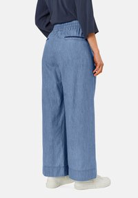 Pantalones de pierna ancha de color azul claro con cintura elástica y bolsillos laterales, hechos de una mezcla de algodón texturizado. Zapatillas blancas llevadas con ellos.