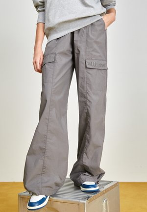 Pantalones cargo grises con bolsillos laterales, corte holgado y puños elásticos. Hechos de tejido ligero, combinados con zapatillas azules y blancas.