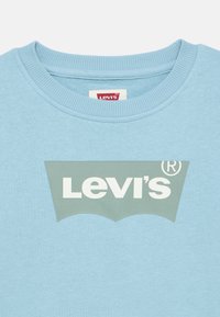 Ανοιχτό μπλε φούτερ με ριγέ λαιμόκοψη τύπου crew. Διαθέτει μεγάλο γκρι λογότυπο Levi's με λευκή περίγραμμα και σχεδιασμό με φθορές.