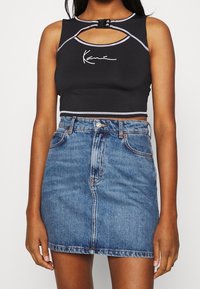 Svart kortärmad crop-top med ett nyckelhål och grå detaljer, kombinerad med en högmidjad blå denimkjol med en framseam och fickor.