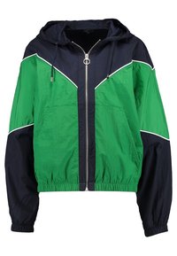 Hættejakke i vindafvisende materiale med fuld frontlynlås, elastisk talje og manchetter, farvesplittet i grøn og marineblå med hvide kantdetaljer.