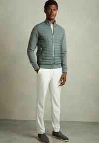 Jachetă căptușită cu fermoar în gri, cu un finisaj neted, asortată cu pantaloni albi personalizați și pantofi gri slip-on. Design simplu și linii curate.