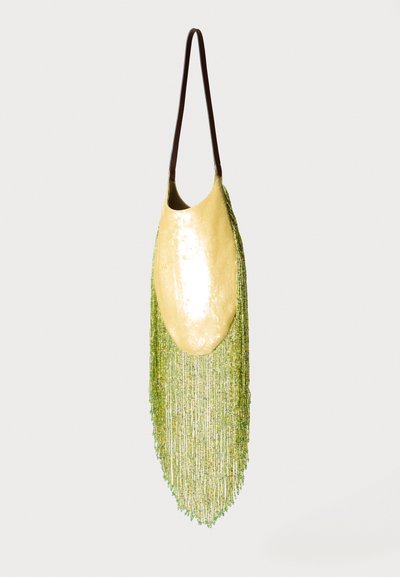 Żółta torebka z cekinami z długimi zielonymi frędzlami z koralików i cienkim ciemnobrązowym paskiem na ramię, wisząca na jednolitym tle.