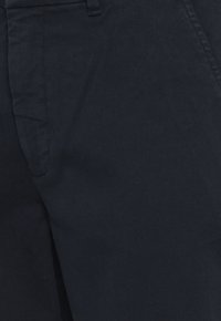 Pantalons bleu foncé en tissu texturé, avec un devant plat et des poches latérales, offrant une finition lisse et une coupe ajustée.