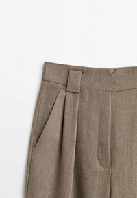 Pantalon plissé marron avec une texture lisse, une coupe ajustée, des passants à la taille et des poches latérales pour plus de fonctionnalité.