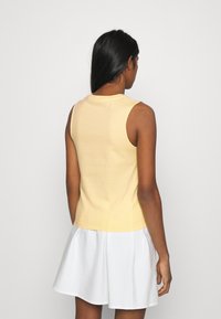 Gul ärmlös topp med en figurnära design och rund halsringning, kombinerad med en vit kjol. Slät tygtextur.