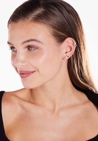 Zilveren oorcuff en stud oorbellen, met een minimalistisch ontwerp, gladde texturen en kleine sprankelende accenten. Huidtint lijkt natuurlijk.