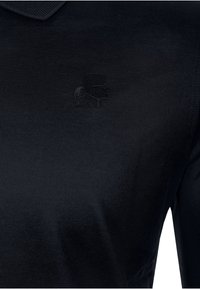 Polo shirt nera realizzata in cotone morbido, con un logo embossato discreto sul lato sinistro del petto e un design del colletto tradizionale.
