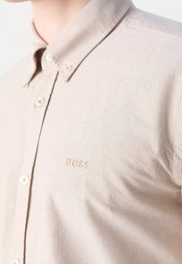 Beige korte mouwen overhemd met knopen, gemaakt van geweven stof, met een klein geborduurd "BOSS" logo en een standaard kraag met contrasterende knopen.