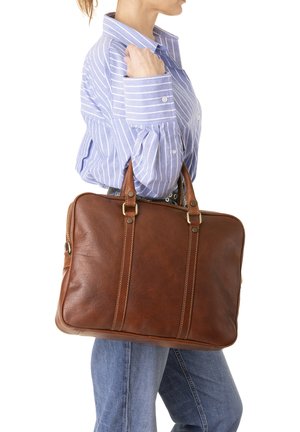 Persoon in lichtblauw gestreept overhemd en spijkerbroek draagt een grote bruine leren aktetas over de schouder.
