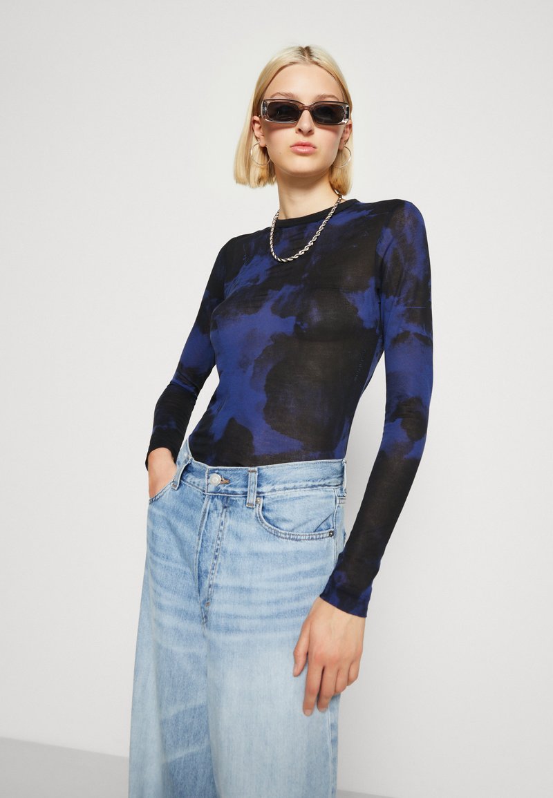 Długi rękaw bluzki w granatowym wzorze tie-dye, wykonanej z lekkiego materiału. W połączeniu z jasnoniebieskimi, wysokimi dżinsami.