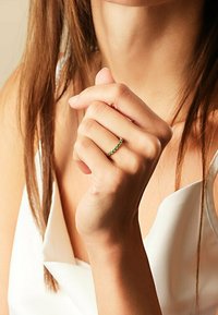 Goldring mit abwechselnd grünen Edelsteinen, dünnes Banddesign, getragen an einer Hand vor einem hellen Hintergrund, mit glatter Hautstruktur.