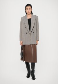 Gray pinstripe double-breasted blazer, black tank top, brown skirt, and black knee-high boots. Model holds a small black handbag.