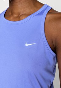 Αμάνικη φανέλα Nike σε ανοιχτό μωβ ύφασμα με λεία υφή και στρογγυλή λαιμόκοψη, με λευκό λογότυπο στο αριστερό μέρος του στήθους.