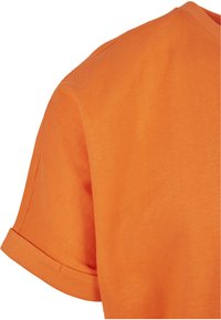 Tricou cu mâneci scurte din bumbac portocalie strălucitoare. Guler rotund cu mâneci răsucite și textură netedă. Fără modele sau accesorii vizibile.