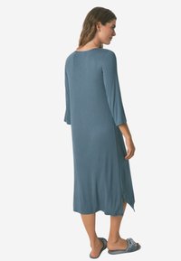 Abito lungo blu a coste con maniche a tre quarti, fessure laterali e taglio rilassato. Tessuto liscio con una leggera lucentezza. Indossato con sandali scivolati.
