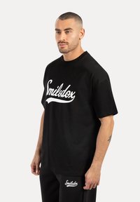 Svart bomulls t-shirt med en vit 'Smilodox'-logotyp framtill. Har en avslappnad passform och korta ärmar, tillsammans med matchande svarta byxor.