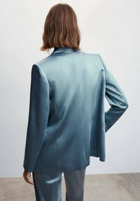 Blazer en satin bleu clair au design structuré, avec des revers crantés et des manches longues. Doté d'une fente unique à l'arrière et d'une texture lisse.