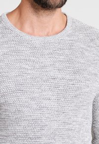 Maglione grigio lavorato a maglia con scollo rotondo e motivo testurizzato. Il tessuto è leggermente ruvido con una maglia larga.