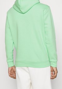 Mintgrön hoodie med en kenguruficka, texturerat tyg och ribbade muddar. Har en huva och en avslappnad passform, tillsammans med vita byxor.