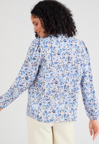 Lichte, langluit blouse in een blauw, roze en crèmekleurig bloemenpatroon. Zachte stof met geplooide schouderdetails en een ronde zoom.