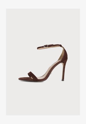 Une sandale à talon haut en daim marron unique avec bout ouvert, bride à la cheville et fermeture à boucle sur fond blanc uni.