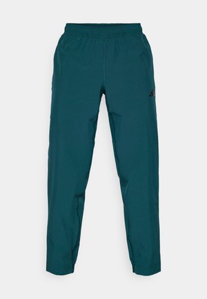 Tirkizne sportske hlače s elastičnim pojasom, suženim nogavicama i crnim logotipom. Izrađene su od glatkog, laganog materijala.