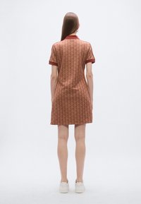 Rövid ujjú barna polo ruha geometriai mintával, piros gallérral és mandzsettával. A szövet texturált hatású, testhez simuló szabással.