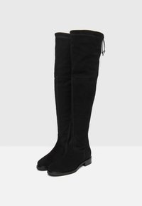Botas negras sobre la rodilla de ante, con una textura suave, puntera redonda y un tacón bajo, además de un cordón en la parte superior.