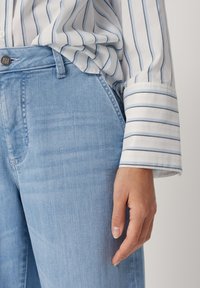 Světle modré džíny s volným střihem, doplněné bílou košilí se světle modrými pruhy a vyhrnutými lemy rukávů.