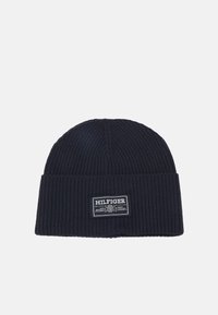 Berretto lavorato a maglia di colore navy con texture a coste e risvolto. Presenta un'etichetta bianca con il nome e il logo del marchio sulla parte anteriore.