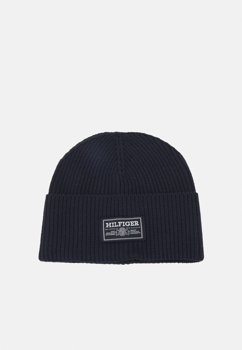 Berretto lavorato a maglia di colore navy con texture a coste e risvolto. Presenta un'etichetta bianca con il nome e il logo del marchio sulla parte anteriore.