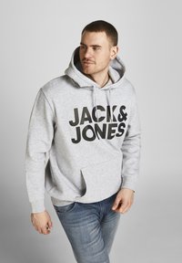 Grijze hoodie met een groot zwart "JACK & JONES" logo, koordkapuchon en kangoeroezak. Materiaal lijkt zacht en gestructureerd.