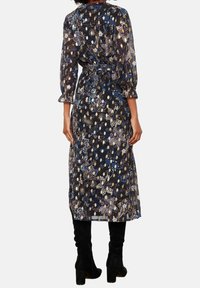 Žena v černých květinových midi šatech s dlouhými rukávy a černých vysokých botách na podpatku, viděná zezadu.