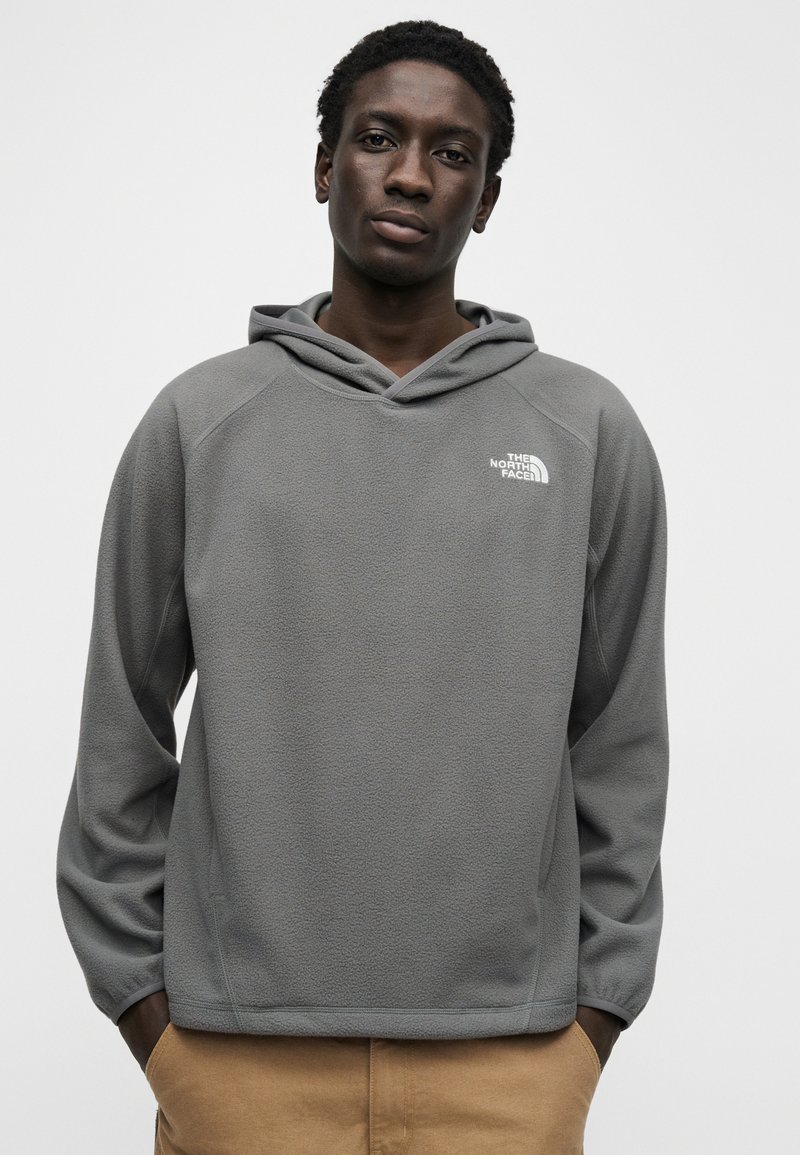 Gray fleece pullover with hood, featuring raglan sleeves and a small white logo on the chest. Soft texture, relaxed fit, and side pockets.