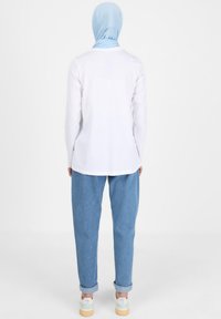 Weißes Langarmhemd mit gerader Schnittführung, kombiniert mit lockeren, hellblauen Jeans und weißen Schuhen mit pastellfarbenen Akzenten.