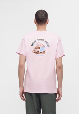 Άνδρας που φορά ένα ανοιχτό ροζ T-shirt με γραφικό ενός παγωτατζίδικου φορτηγού και το κείμενο "Treat your sole!" στην πλάτη.