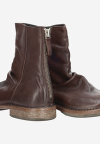 Bottines en cuir marron avec une fermeture éclair sur le côté, texture douce et semelle en bois usée, arborant un design légèrement affaissé.
