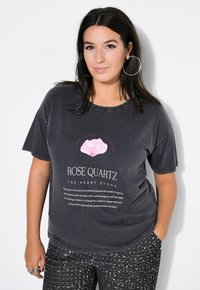 Grijze oversized t-shirt met een roze rozenkwarts grafiek en witte tekst. Gepaard met zwarte paillettenbroek met een glanzende textuur.
