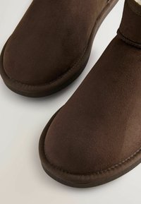 Pruunid nahast ankle-bootsid sileda tekstuuri, ümmargune varvas ja õmblustekitus taldadel. Kummi välistald, mis tagab haarde ja vastupidavuse.
