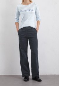 Sininen ja valkoinen raitapaitainen pitkähiha, jossa on "Marc O'Polo" -teksti, yhdistetty tummanharmaisiin suoriin housuihin ja mustiin kenkiin.