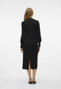 Schwarzes, figurbetontes Kleid mit langen texturierten Ärmeln, Schlitz bis zum Knie hinten und aus glatter Strickware. Schlichter Ausschnitt und elegante Silhouette.