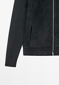 Giubbotto nero con davanti in suede liscio e maniche a coste testurizzate. Dotato di zip metallica e tasche laterali.