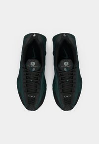 Sapatilhas Nike Shox com parte superior em preto e verde-água, design texturizado, painéis em malha e pormenores metálicos; apresentam fecho de atacadores e detalhe do logo.