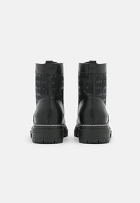 Botas de tobillo de cuero negro con un panel de tela negra texturizada que presenta un estampado de logotipo repetido, suela gruesa y tiradores en la parte posterior.