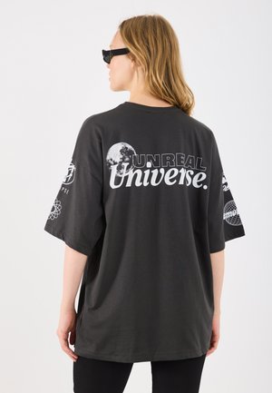 T-shirt oversized preta com gráfico "UNREAL Universe", design de lua e padrões abstratos nas mangas. Tecido de algodão suave.