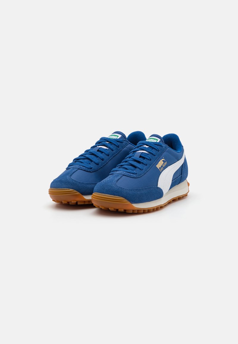 Zapatillas de ante azul con acentos blancos, tejido texturizado, suela de goma y diseño tradicional con cordones, que presentan un logo en el lateral.